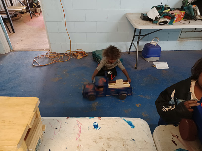A child playing with their wooden toy truck and seeing if it needs more paint at A child painting a wooden toy truck at the Family Day at Manyallaluk